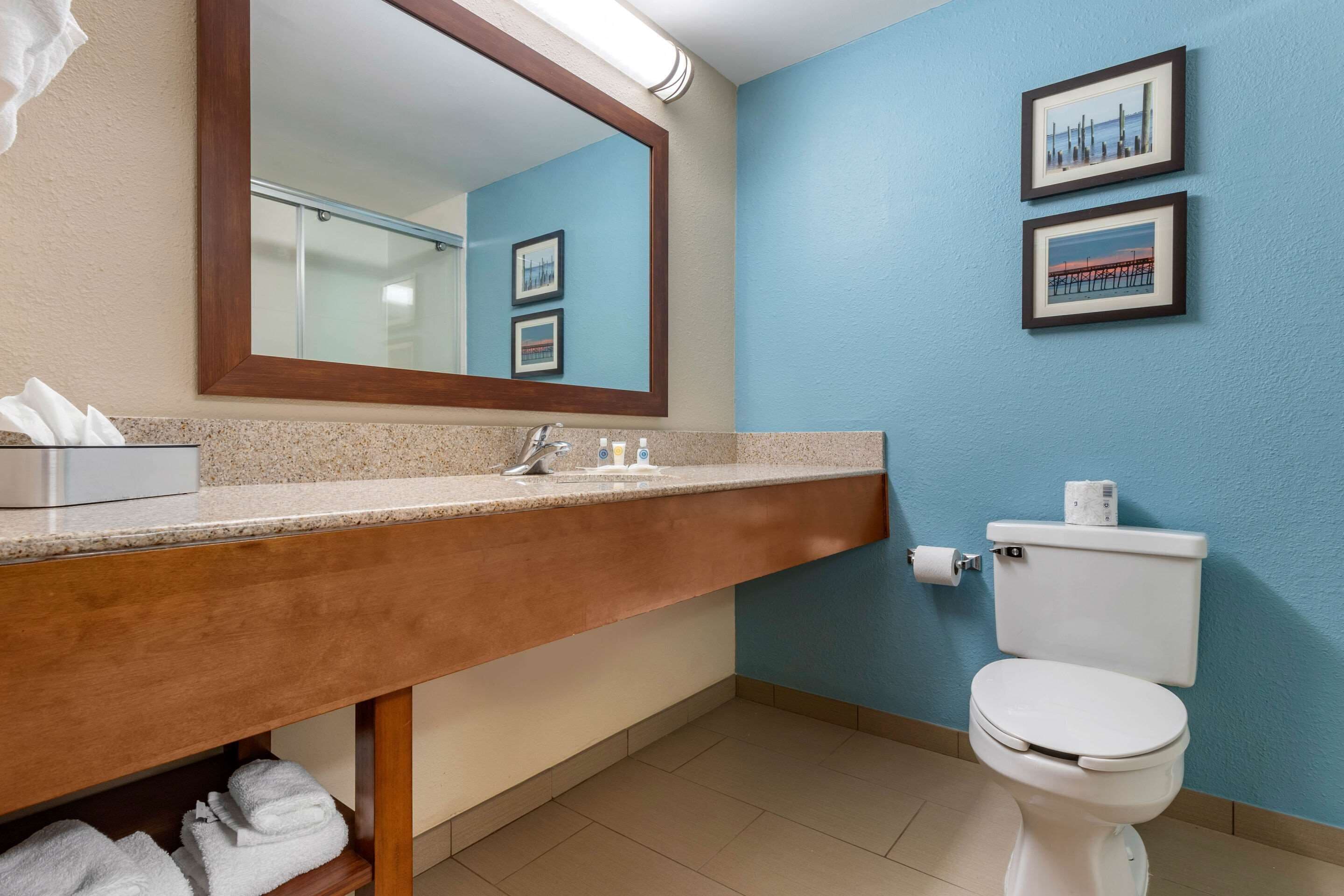 Un baño con tocador de madera, lavamanos, inodoro y dos cuadros en la pared.