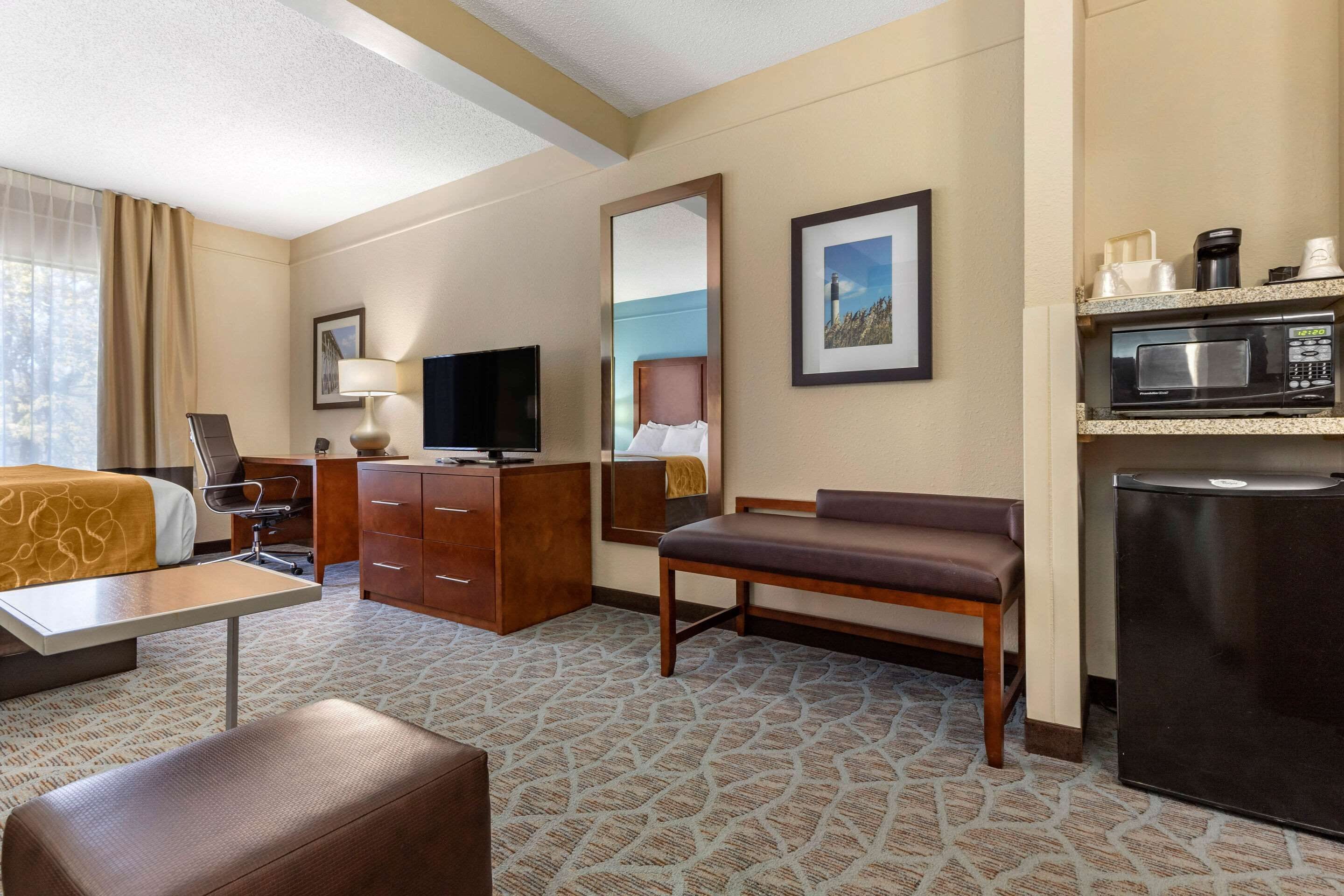Een hotelkamer met een bed, een bureau, een stoel, een televisie, een spiegel, een koelkast en een magnetron.