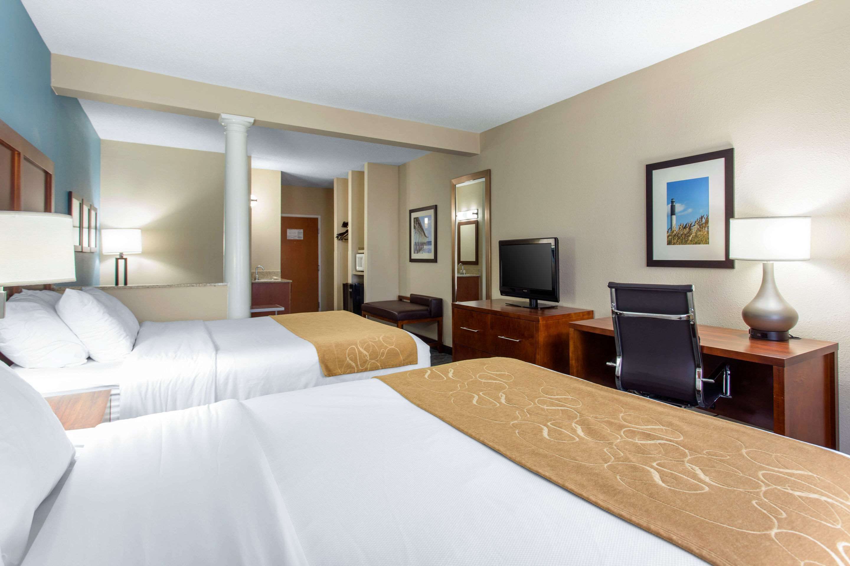 A hotel room with two beds, a desk with a computer, a TV, and a chair.