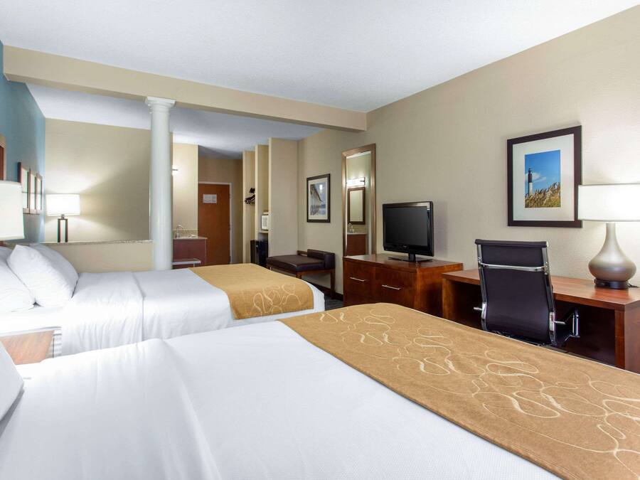 A hotel room with two beds, a desk with a computer, a TV, and a chair.