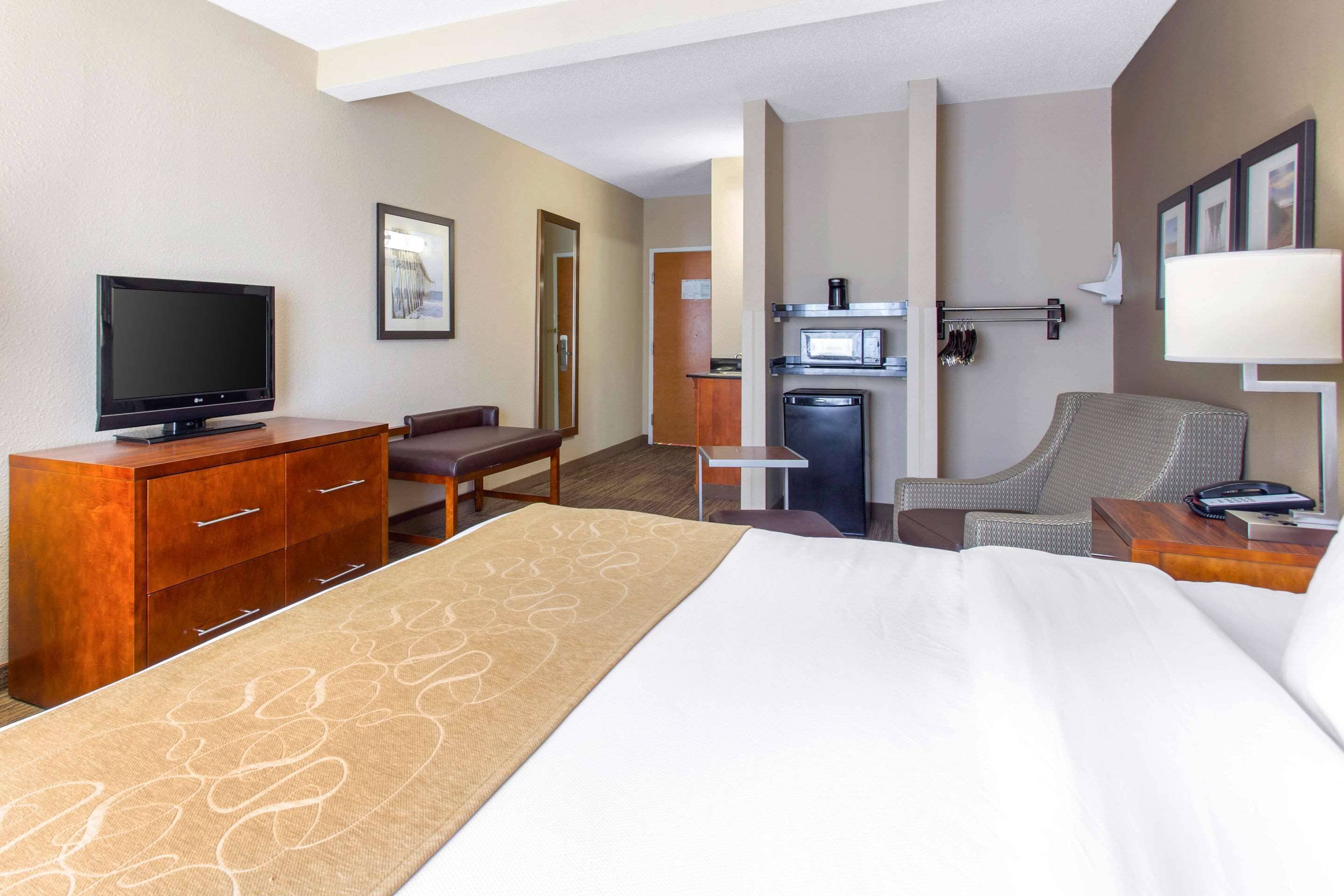 Quarto de hotel com cama, televisão, escrivaninha, cadeira, micro-ondas e frigorífico.