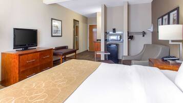 Quarto de hotel com cama, televisão, escrivaninha, cadeira, micro-ondas e frigorífico.