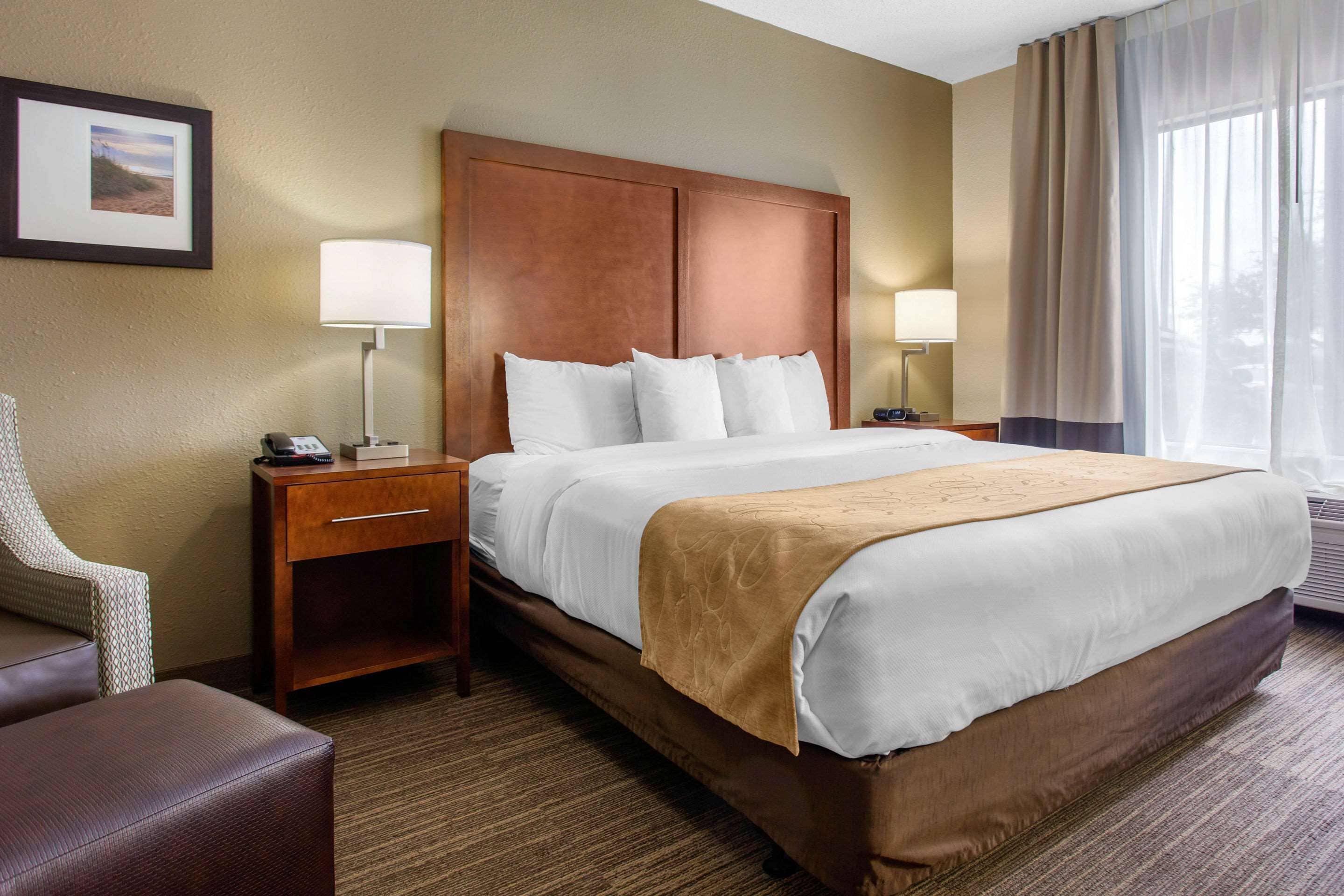 Een hotelkamer met een groot bed, twee nachtkastjes, een stoel en een schilderij aan de muur.