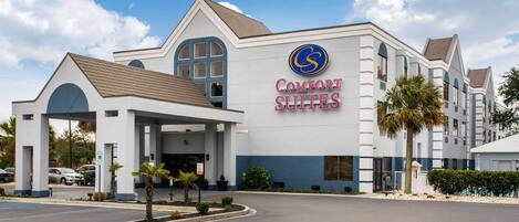 A hotel named Comfort Suites with a modern design, featuring a prominent entrance and a parking area.