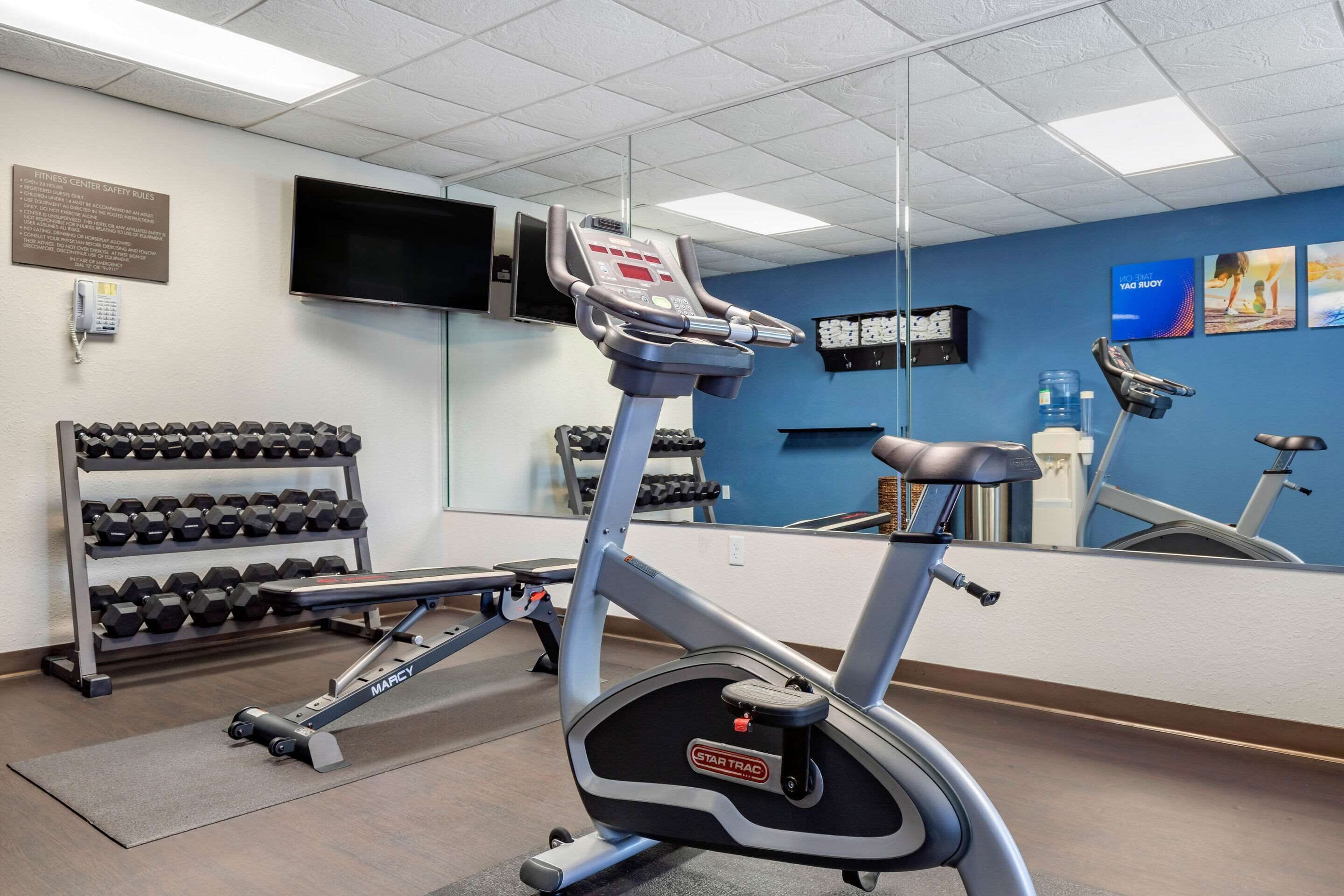 Un gimnasio con cinta de correr, mancuernas y un espejo.