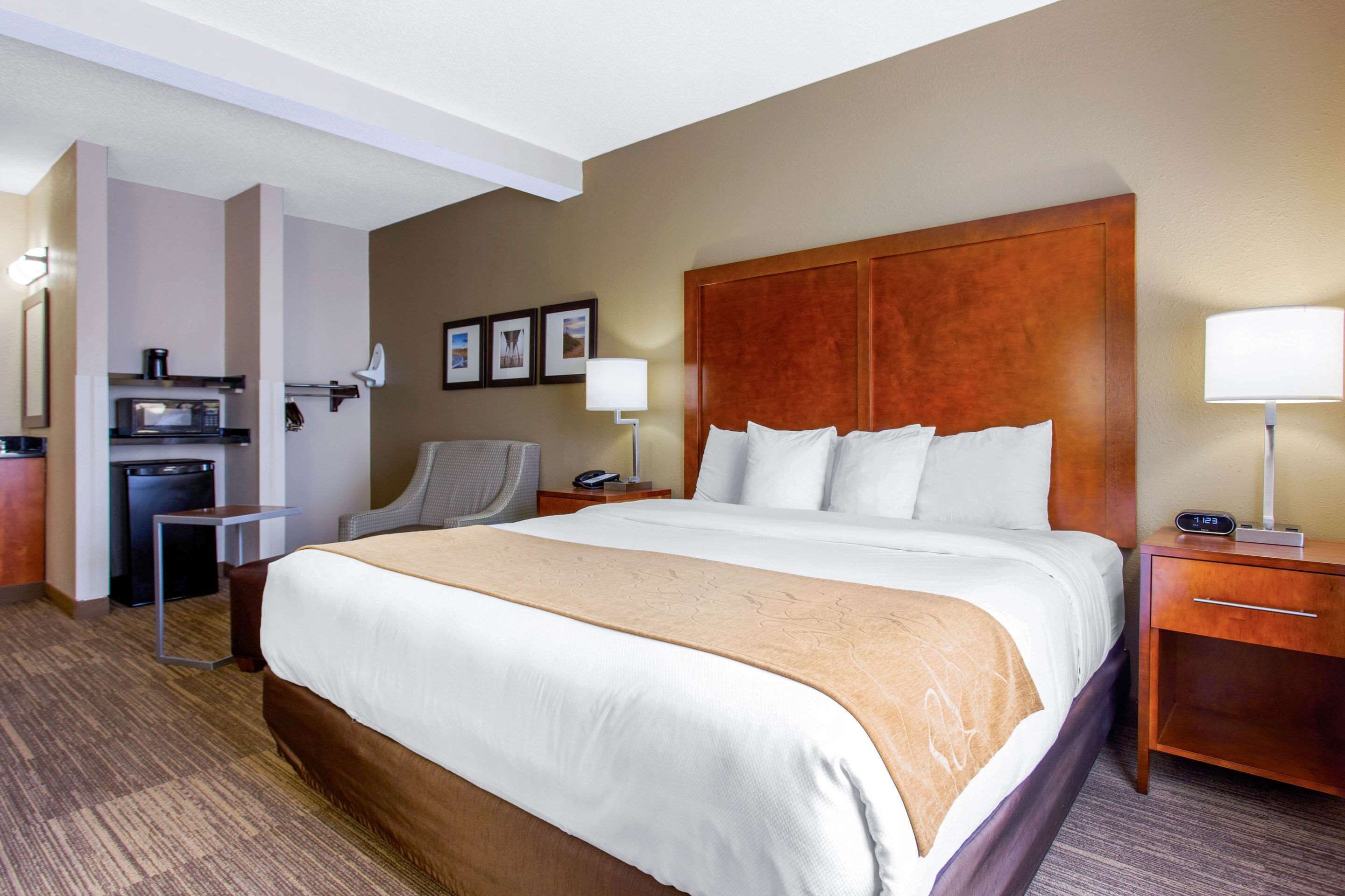 Habitación de hotel con una cama grande, un escritorio con lámpara, una silla, microondas y un refrigerador pequeño.