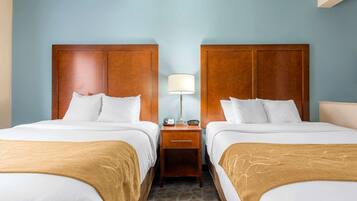 A hotel room with two beds, wooden headboards, a nightstand with a lamp, and a patterned carpet.