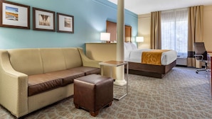 A hotel room with a sofa, a bed, a small table, and a chair. There are three framed pictures on the wall. - Comfort Suites Southport - Oak Island (Southport)