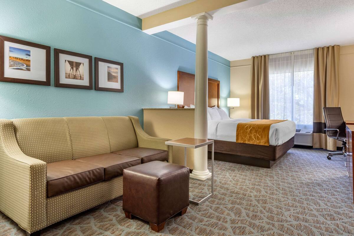 Habitación de hotel con sofá, cama, una mesita y una silla. En la pared, tres cuadros enmarcados.