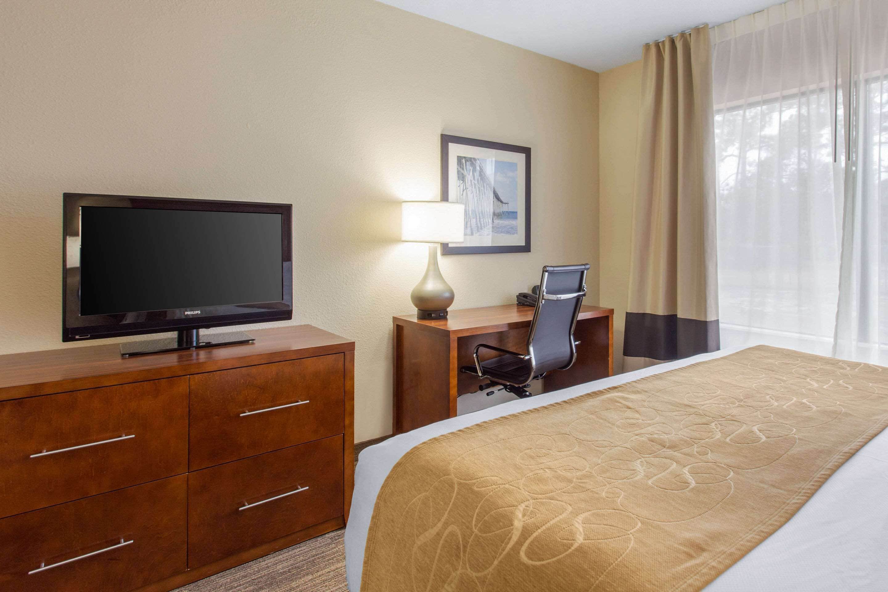 Una habitación de hotel con cama, escritorio, silla, televisor y lámpara.