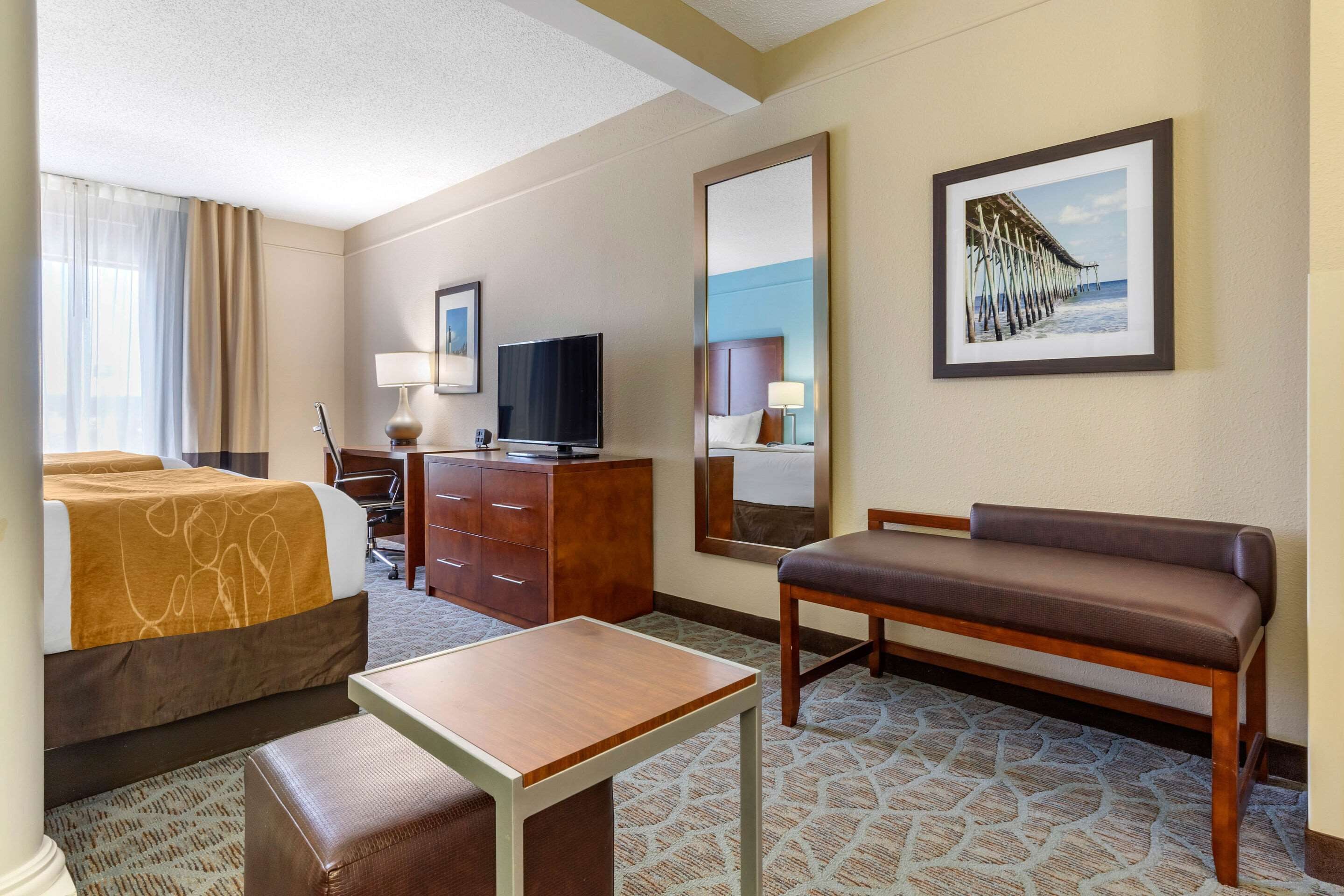A hotel room with a bed, a desk, a chair, a television, a dresser, and a large mirror.