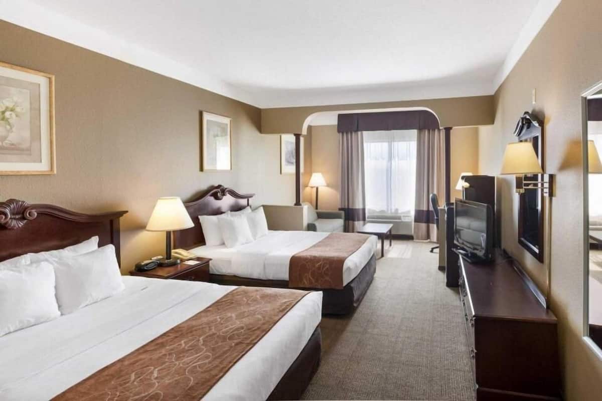Una habitación de hotel con dos camas, un escritorio, un televisor y una ventana con cortinas.