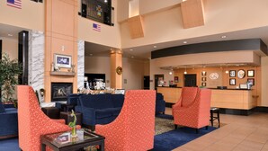 A hotel lobby with a reception desk, seating area with patterned chairs, a fireplace, and American flags.