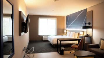 Habitación de hotel con cama, escritorio, silla, mesita, lámpara, televisor y ventana.