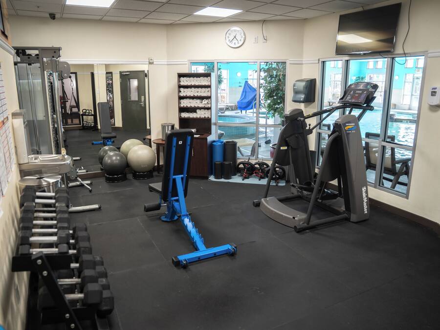 Un gimnasio con equipo de ejercicio, un reloj y una ventana con vista a una piscina.
