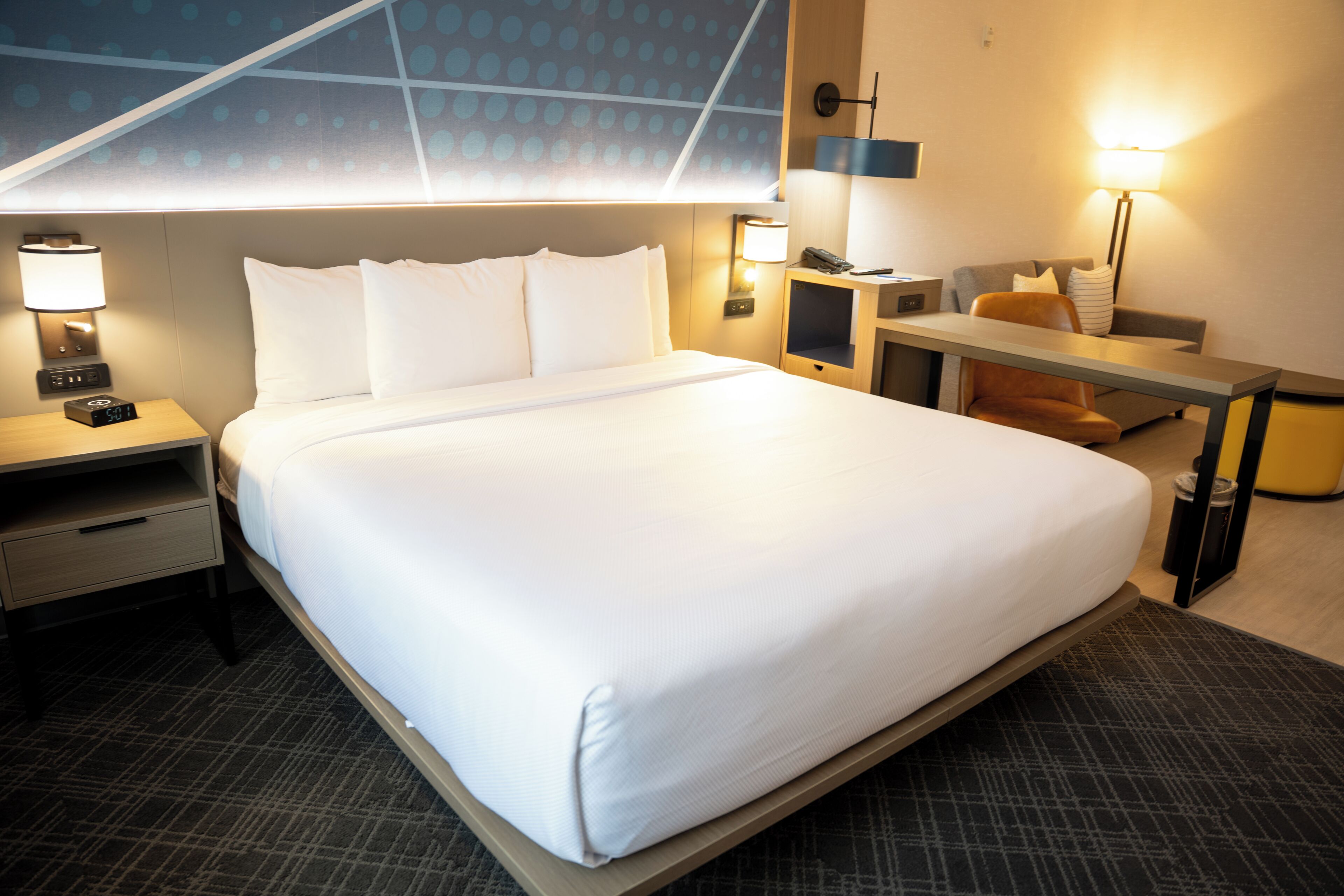 Ett hotellrum med en stor säng, sängbord, ett skrivbord och en stol.
