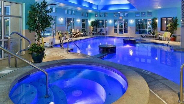 An indoor swimming pool with a hot tub, lounge chairs, and potted plants.