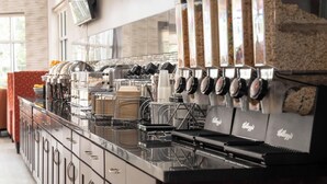 A coffee machine with multiple dispensers, a counter with stacked cups, and a branded coffee bag.