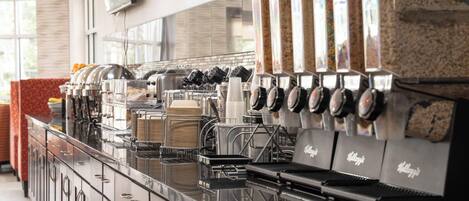 A coffee machine with multiple dispensers, a counter with stacked cups, and a branded coffee bag.