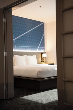 A hotel room with a bed, a nightstand, a lamp, and a view of a blue patterned wall. - Comfort Suites Airport Tukwila Seattle (Tukwila)