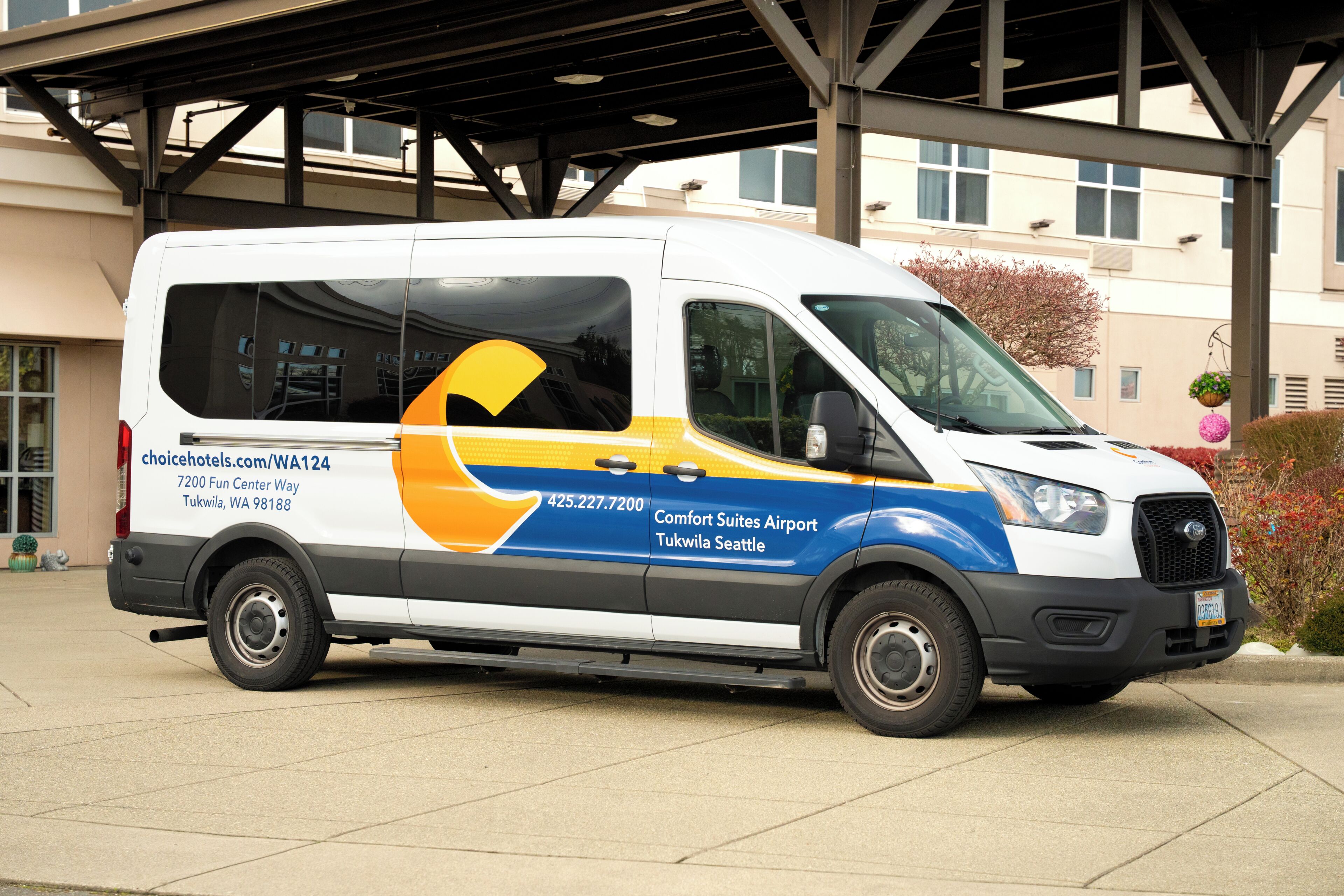 A white van with yellow and blue accents, parked in front of a building with a covered entrance.