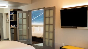 A hotel room with two beds, a television, a bench, and a door leading to a balcony.