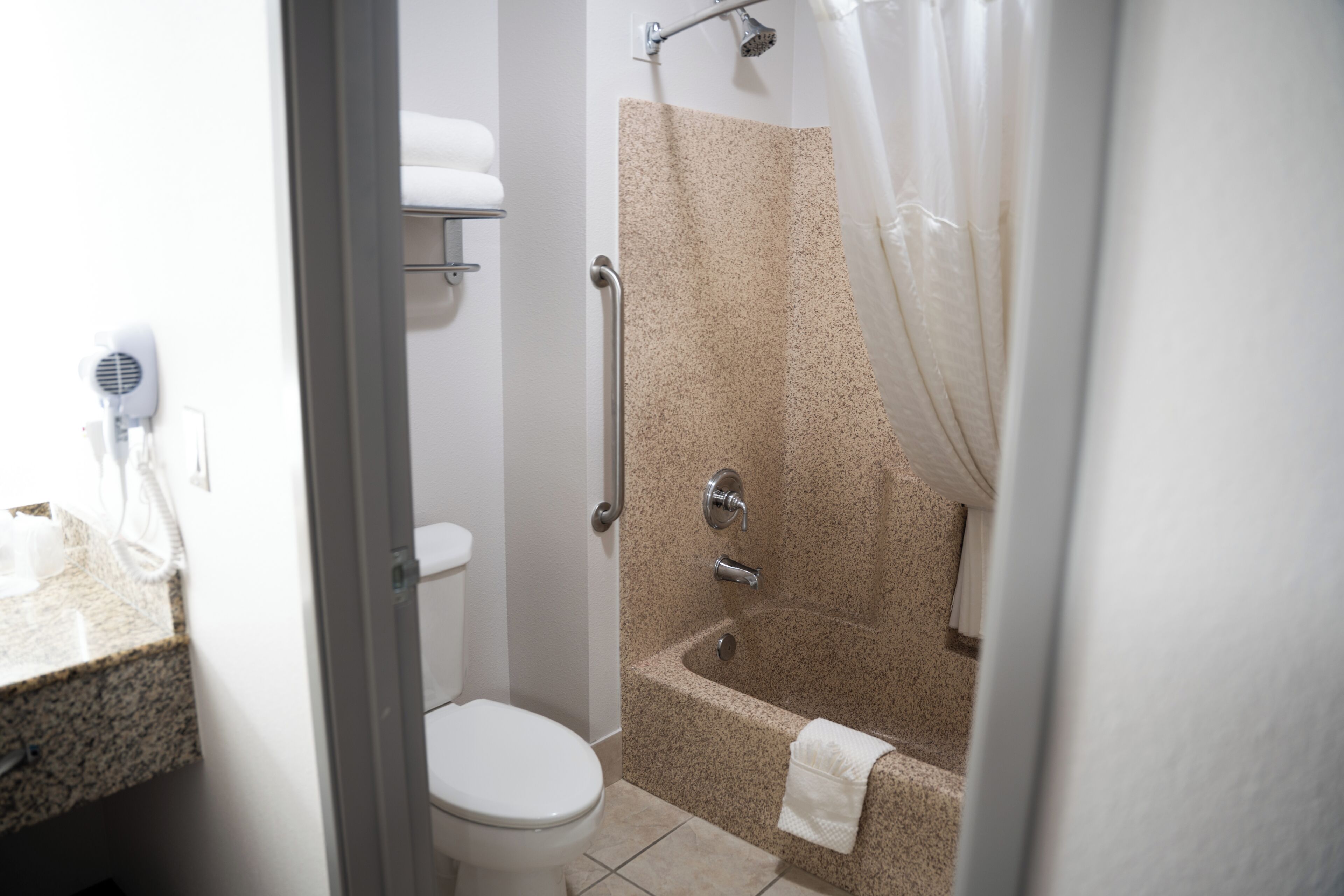 A bathroom with a toilet, a shower with a glass door, a towel rack, and a hairdryer on the counter.