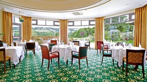 Un comedor con mesas dispuestas para el servicio, amplias ventanas con vistas al exterior y una alfombra estampada.