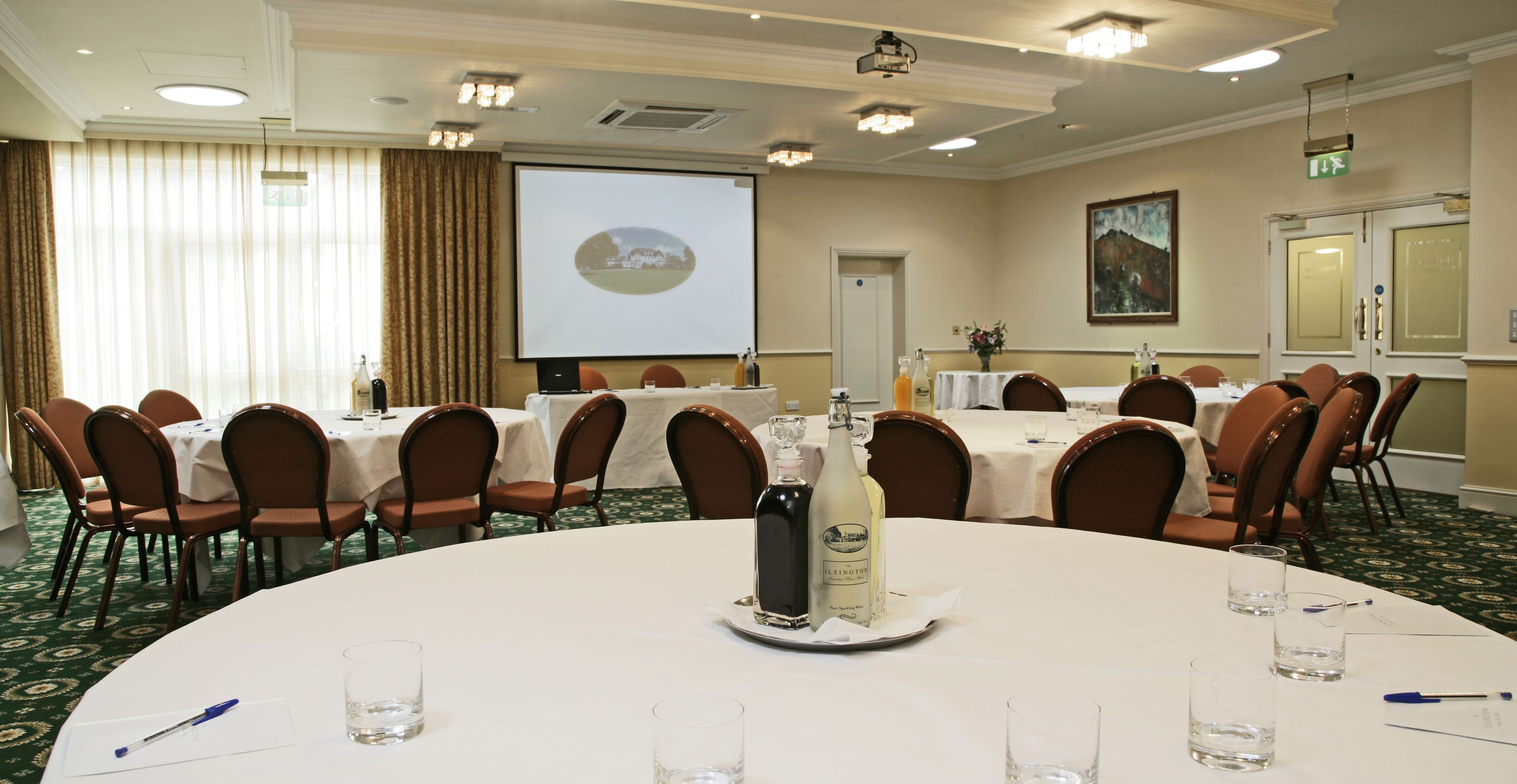 A conference room with round tables, chairs, a projector screen, and a presentation on the screen.