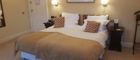 A neatly made bed with a brown blanket, two wall-mounted lamps, a framed picture above the bed, and a bedside table with a tissue box.