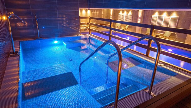 Una piscina interior moderna con agua azul cristalina, barandillas metálicas e iluminación cálida.