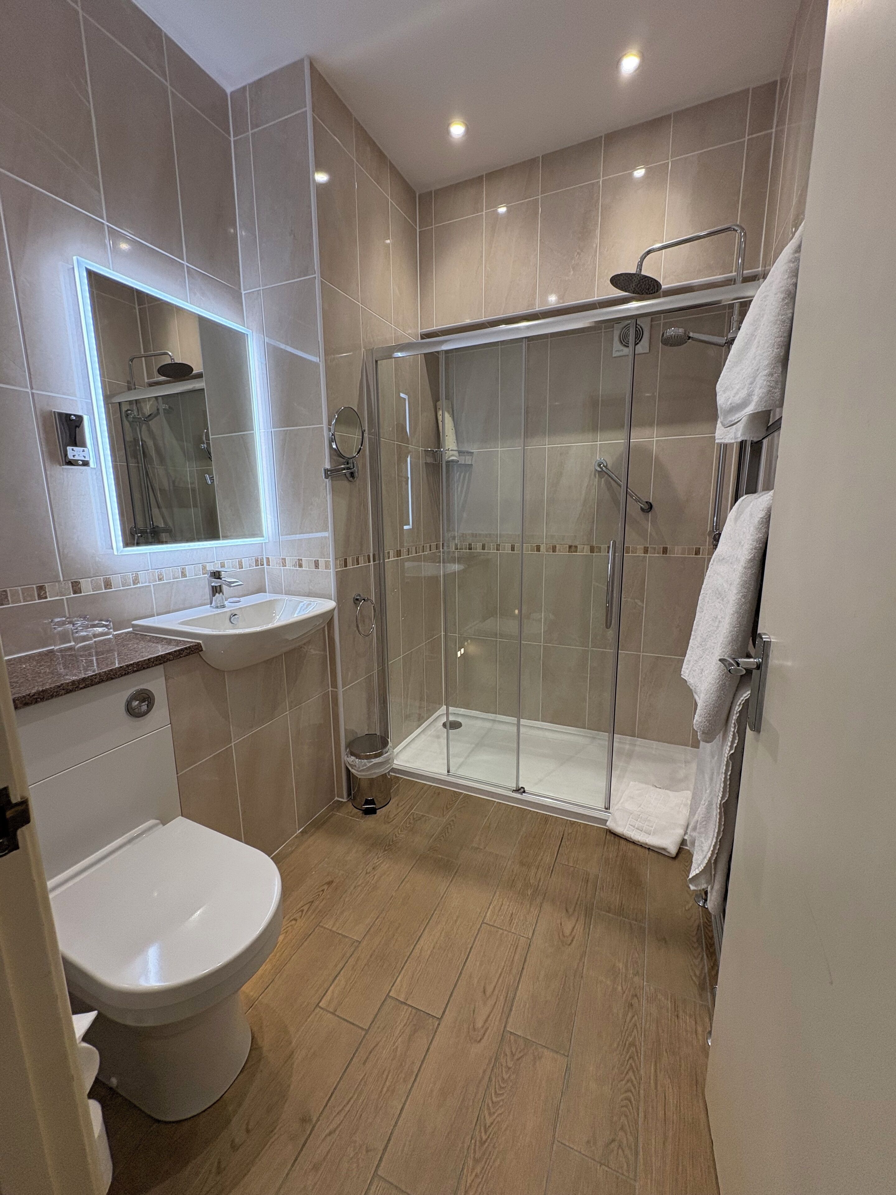 Een moderne badkamer met een douche met glazen wand, een wastafel en een toilet.