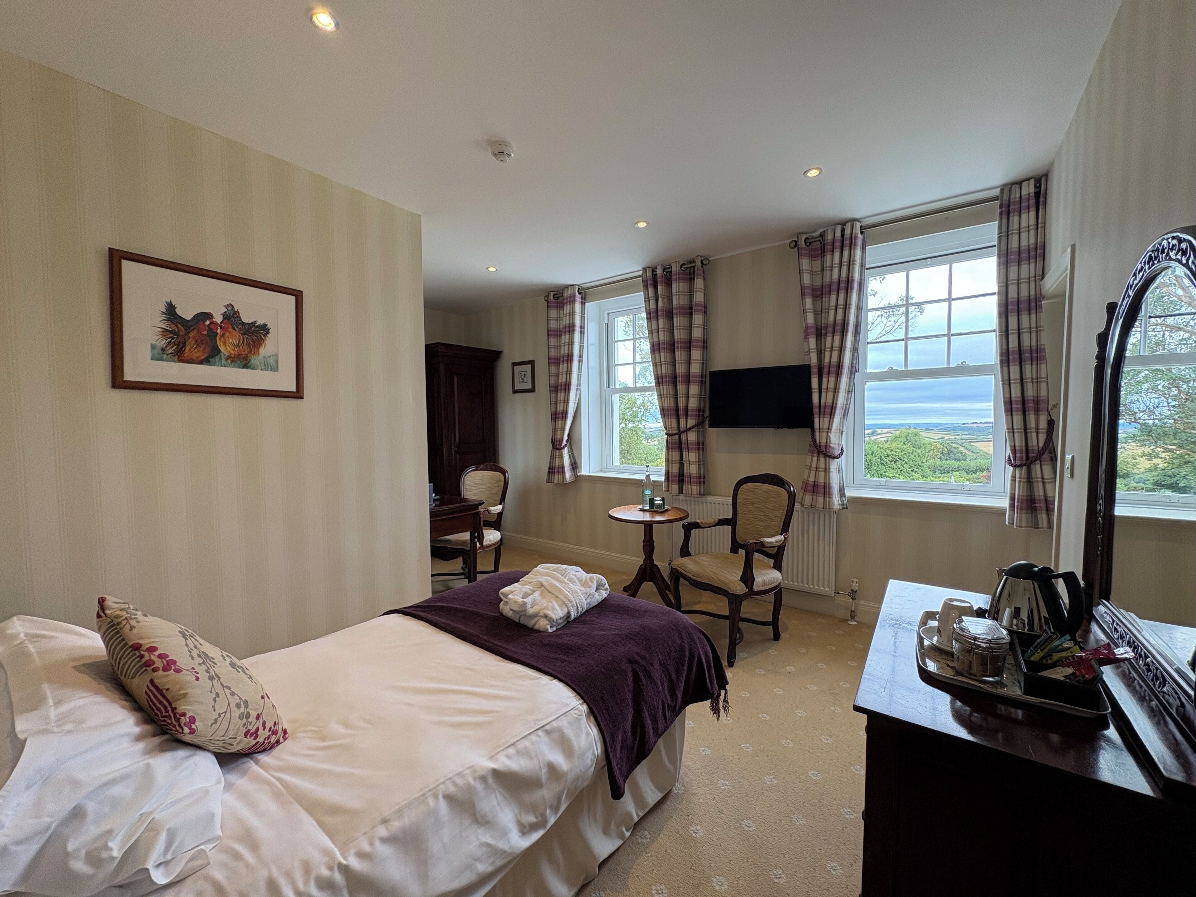 A hotel room with a bed, a desk with a mirror, a chair, a television, and a window with curtains.