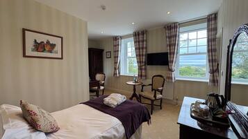 A hotel room with a bed, a desk with a mirror, a chair, a television, and a window with curtains.