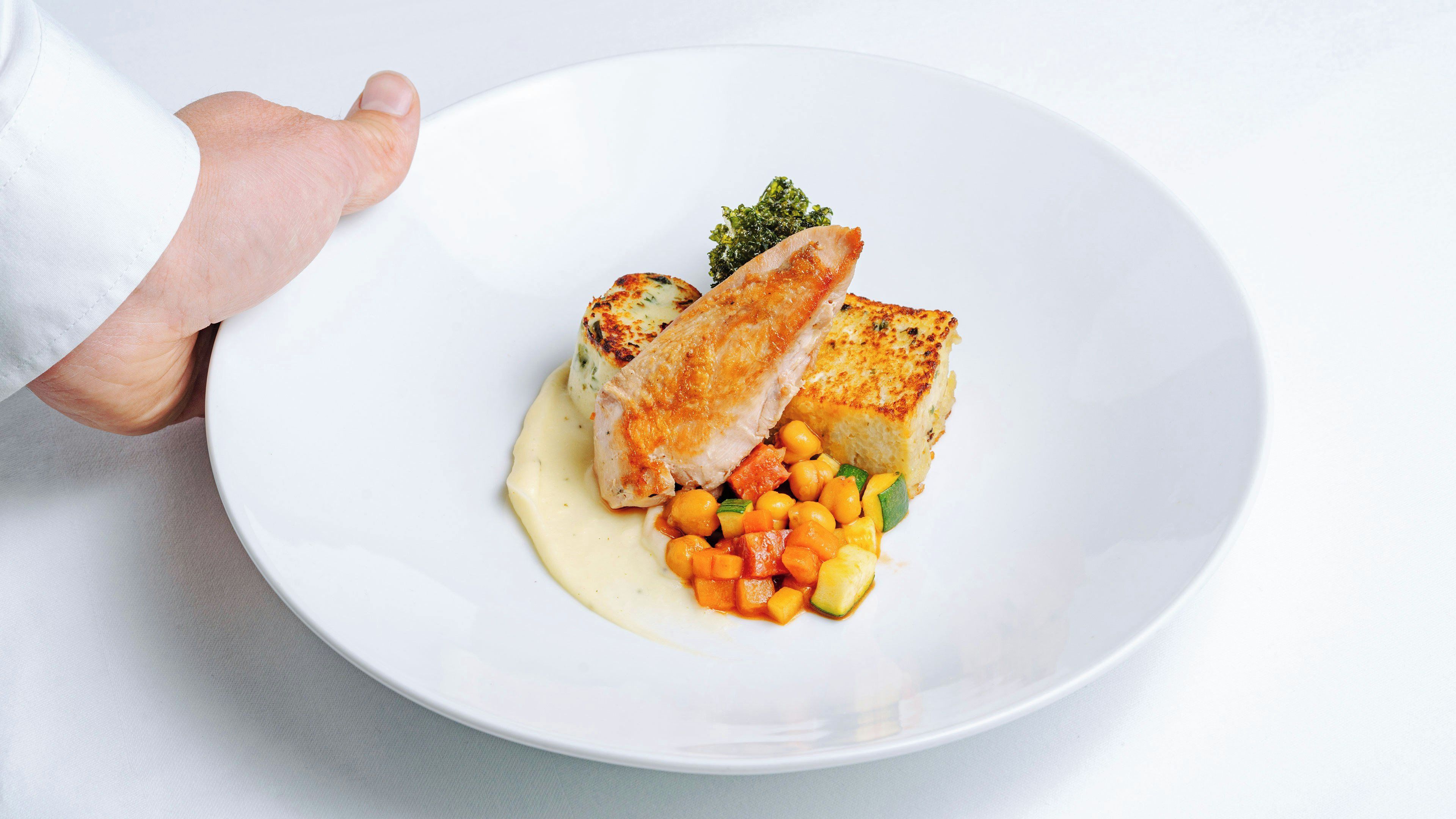 A white plate with a piece of grilled fish, a dollop of sauce, and a side of vegetables.
