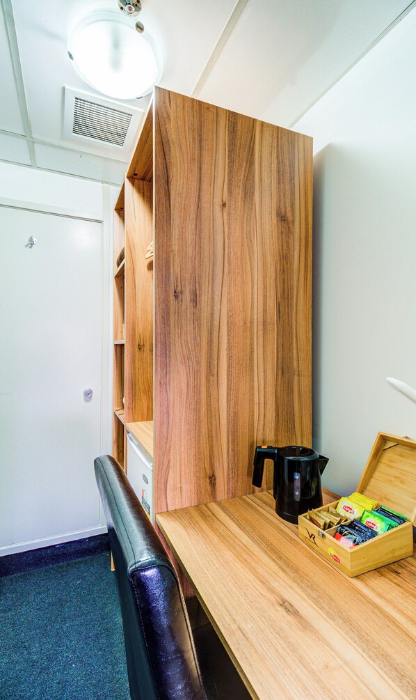 A modern office space with a wooden desk, a black leather chair, a coffee maker, and a box of Lipton tea.