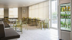 Un comedor moderno con una mesa larga y sillas, un sofá y un refrigerador lleno de bebidas.