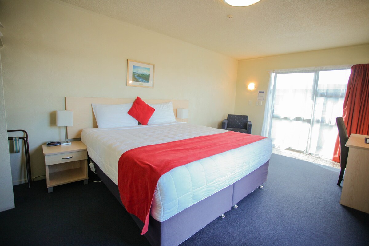 A hotel room with a bed, a nightstand, a desk, a chair, and a window with curtains.