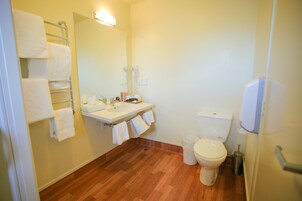 Um banheiro com piso de madeira, pia, vaso sanitário e porta-toalhas com várias toalhas.