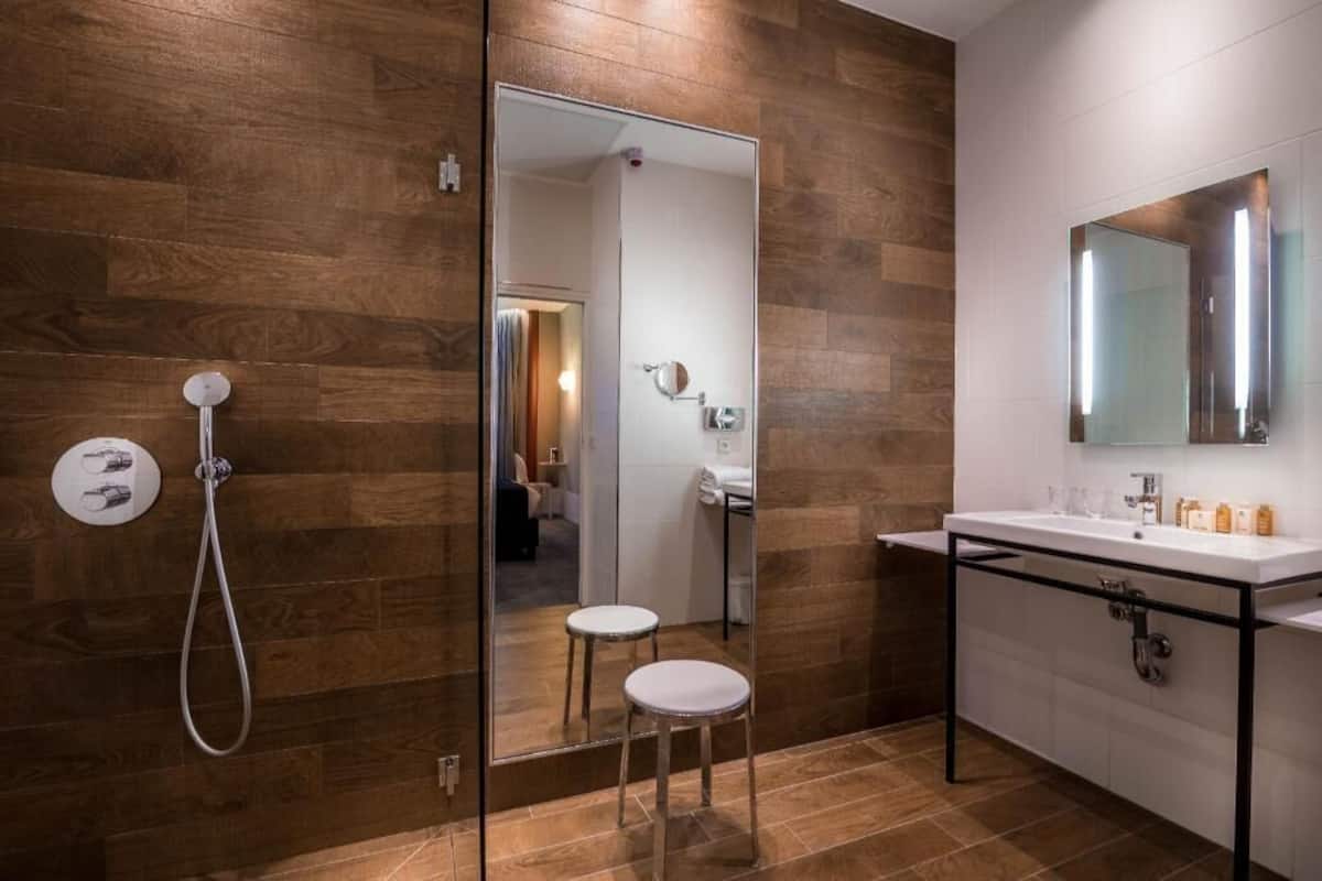 A modern bathroom with a wooden wall, a glass shower enclosure, a white sink, and a mirror.