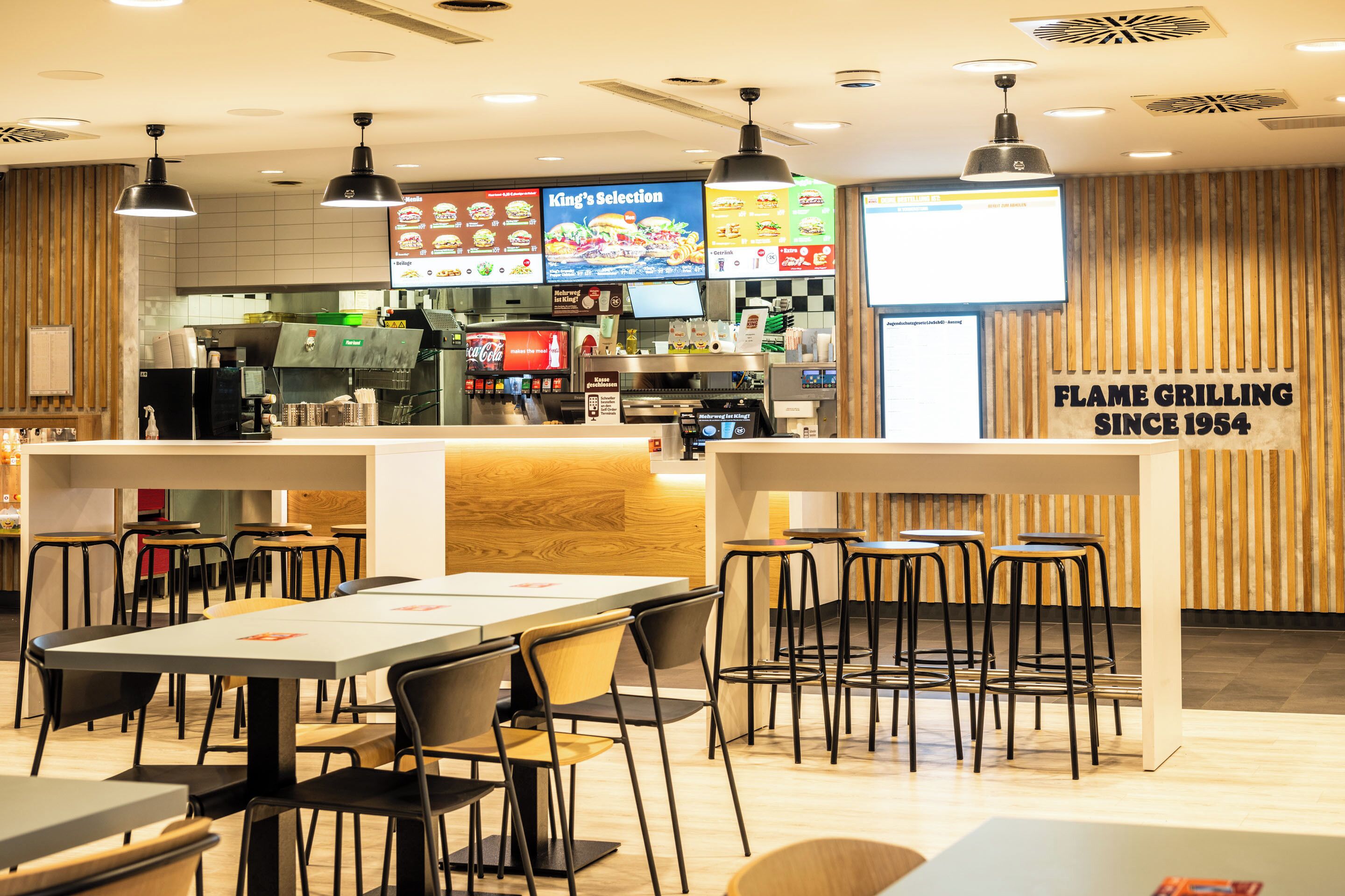A restaurant interior with tables and chairs, a menu board, and a counter with a coffee machine.