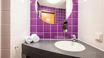 Un baño con un espejo redondo, un lavamanos y dos toallas enrolladas sobre el mostrador.