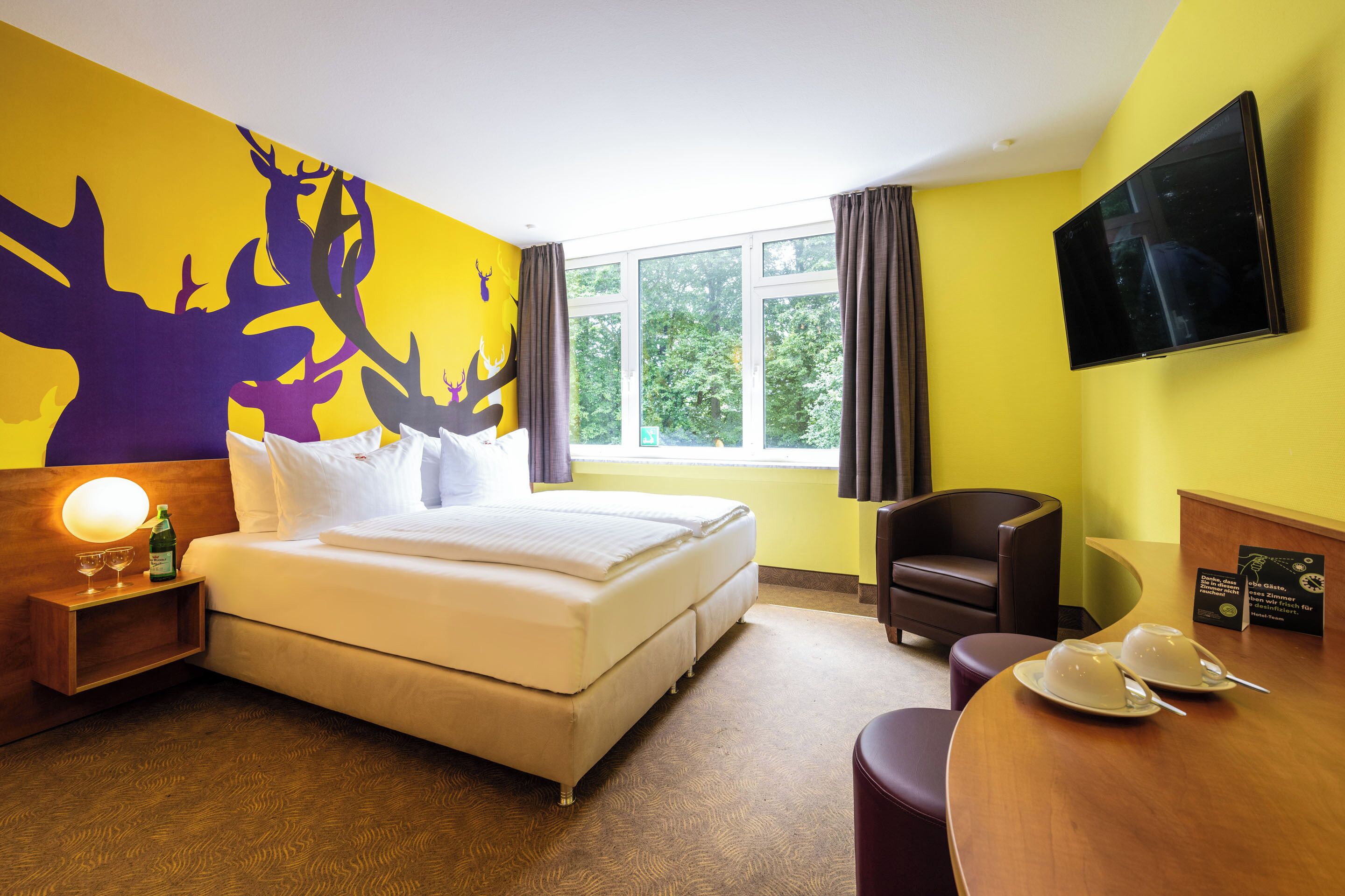 A hotel room with a bed, a desk, a chair, a TV, and a window with curtains.