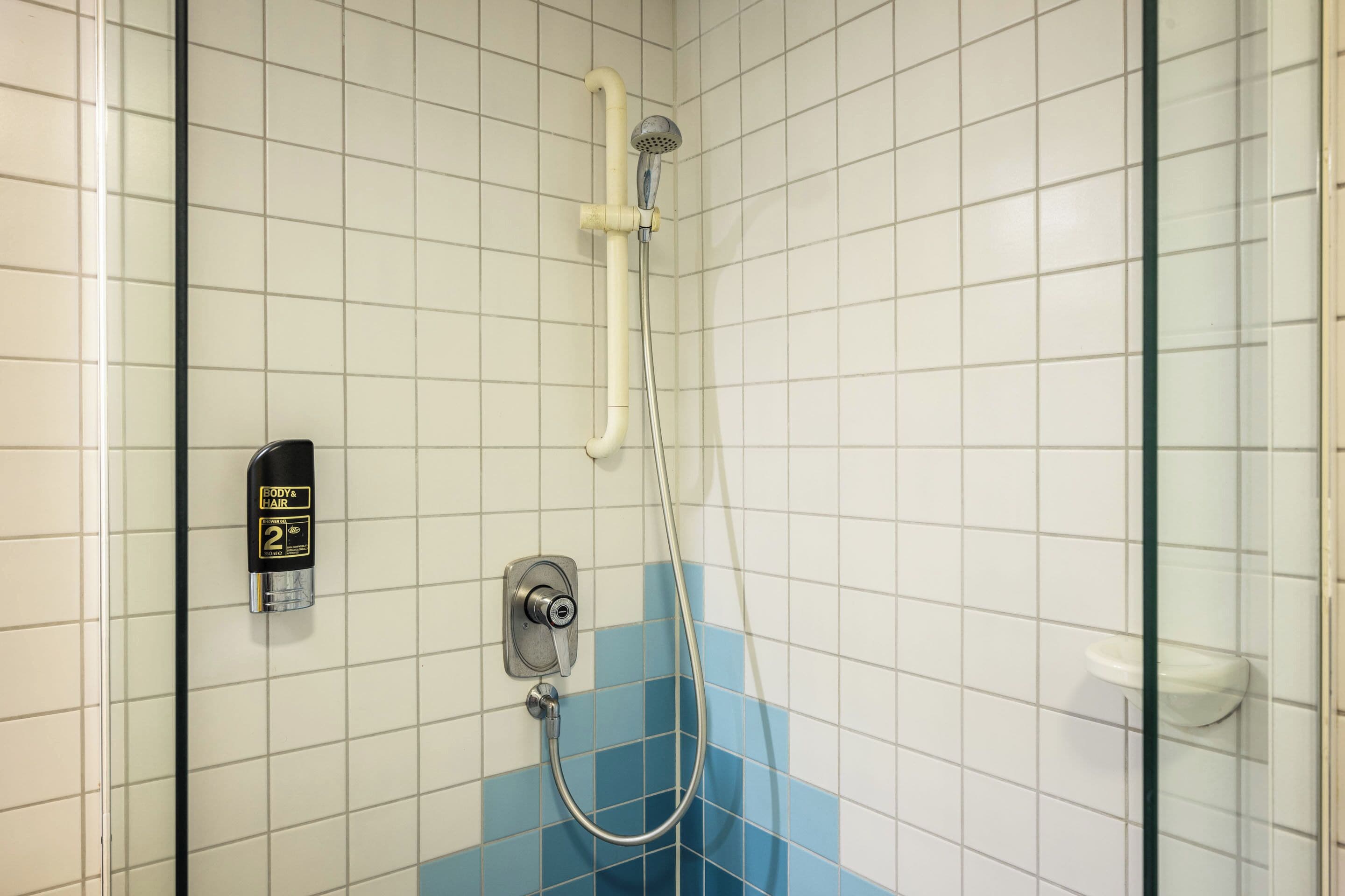 A shower with a handheld showerhead, a soap dispenser, and a control panel.