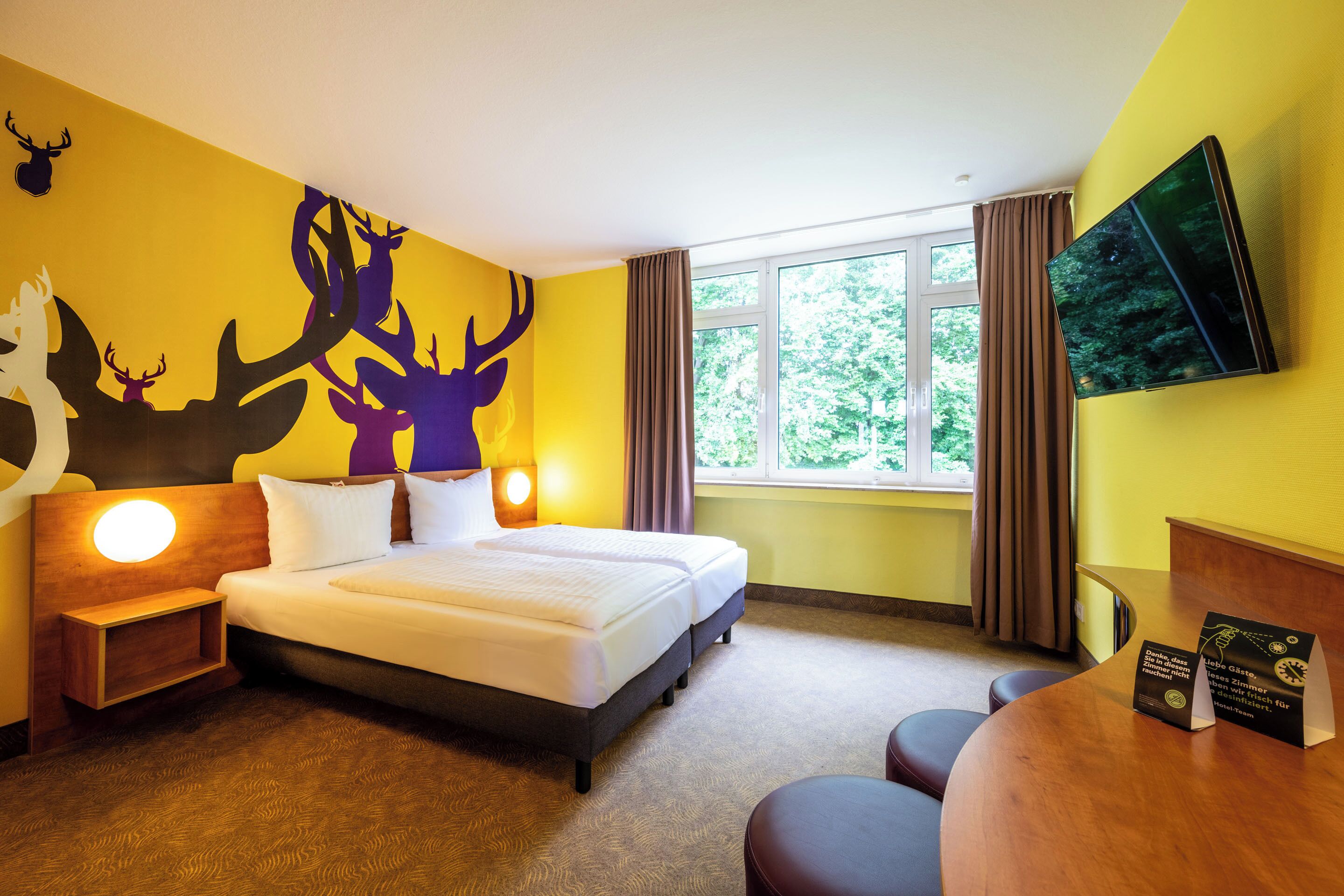 Une chambre d’hôtel avec un grand lit, un bureau, une télévision et une fenêtre avec des rideaux.