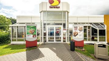 Una tienda Serways con entrada de vidrio, zona de estar al aire libre y carteles promocionales.