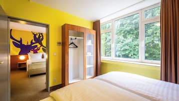 A hotel room with a bed, a wardrobe, a wardrobe with a mirror, a window with curtains, and a door leading to another room.