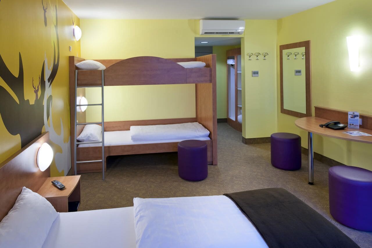 Una habitación de hotel con una cama litera, un escritorio con silla, una mesa redonda y un espejo.
