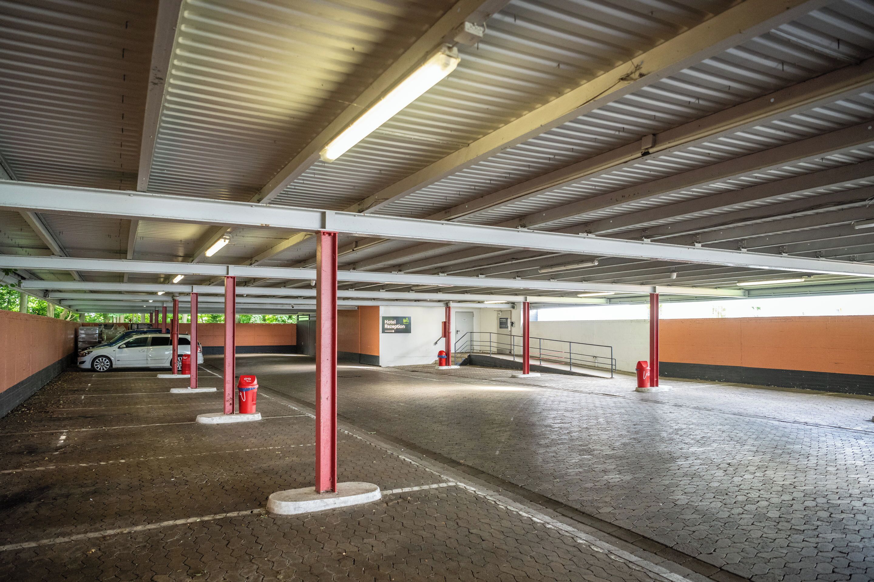 A covered parking area with red pillars, a white car, and a red fire hydrant.