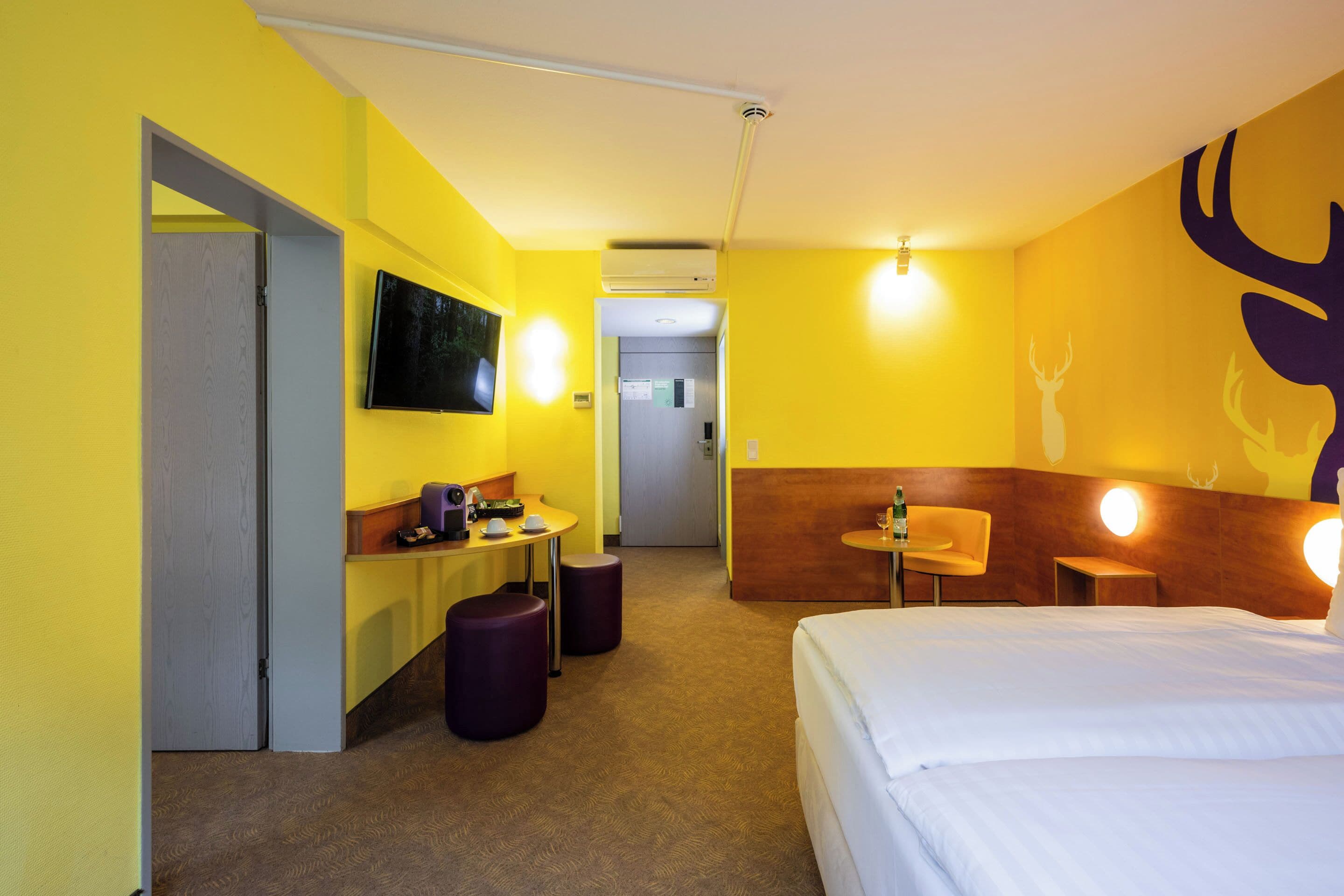 Ein Hotelzimmer mit Bett, Schreibtisch, Stuhl und Fernseher an der Wand.